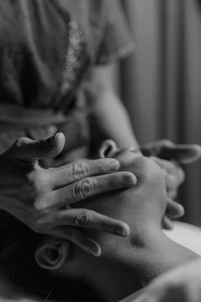 Grayscale Photo of a Person's Hands Massaging a Person's Face