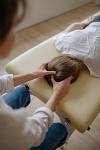 A chiropractor performing a therapeutic head massage on a woman lying on a massage table.